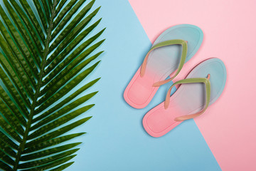 Stylish beach flip-flops on pink and blue pastel background with palm leaf, top view. Summer minimalistic concept with copy space.