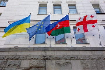 Waved national flags on facade wall with windows. Government or business building of some international organization or company. Flags of Ukraine, EU, Georgia and Azerbaijan