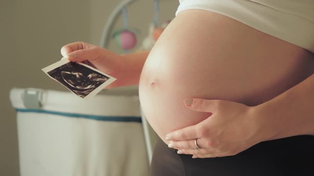 Pregnant lady expecting holding a ultrasound scan picture, closeup