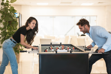 two young colleagues brunette beautiful woman and handsome man playing table football during break at the office looking excited