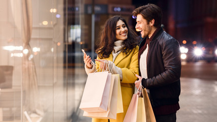 Young couple with shopping bags and smartphone near mall