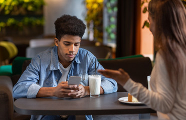 Fototapeta na wymiar Bored black guy looking at smartphone during date time