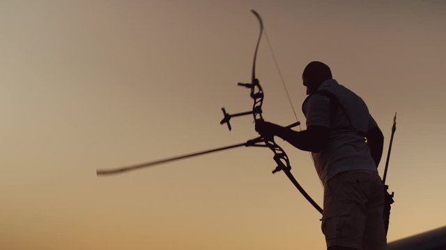 Man shoots a bow. Archery silhouette, sun sets behind the archer