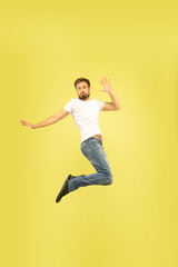 Fototapeta na wymiar Full length portrait of happy jumping man isolated on yellow background. Caucasian male model in casual clothes. Freedom of choices, inspiration, human emotions concept. Gives five, greets, confident.
