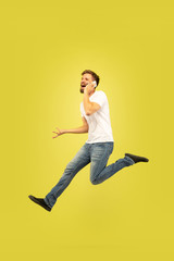 Fototapeta na wymiar Full length portrait of happy jumping man isolated on yellow background. Caucasian male model in casual clothes. Freedom of choices, inspiration, human emotions concept. Hurry up, talking on phone.