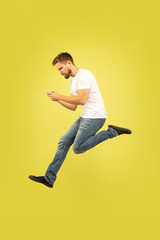 Fototapeta na wymiar Full length portrait of happy jumping man isolated on yellow background. Caucasian male model in casual clothes. Freedom of choices, inspiration, human emotions concept. Winning in sport bet.