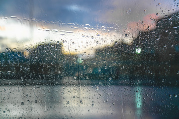 Raindrops on a car glass against a blurred background with a view of the city and the lights of cars.