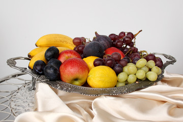 beautiful fruits in a dish, apples, plums, lemons, bananas, purple figs, clusters of black and green grapes with drops, splashes of water, close-up, concept vitamins, healthy eating, copy space