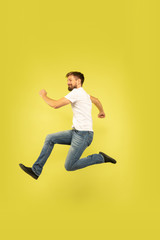 Fototapeta na wymiar Full length portrait of happy jumping man isolated on yellow background. Caucasian male model in casual clothes. Freedom of choices, inspiration, human emotions concept. Running happy.