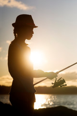 angler fisherman girl with rod and reel catch fishes in summer at sunset