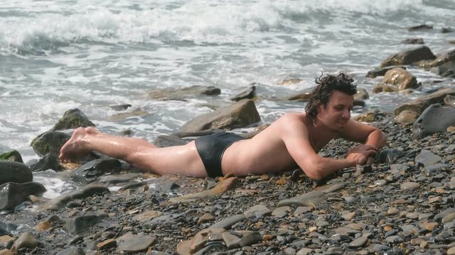 Happy man is laying in sea waves in storm on stone beach