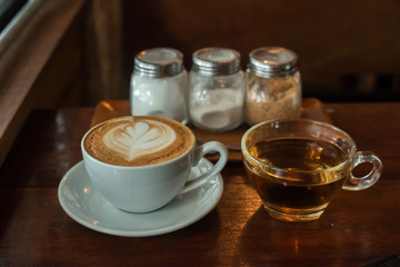 A latte coffee cup is placed at the table, with condiments and tea cups on the side.