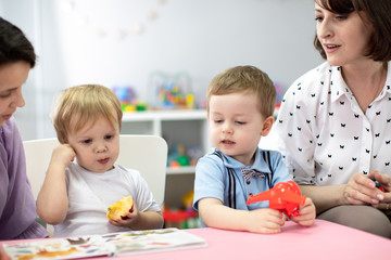 Kids view images in book with adults at table in nursery