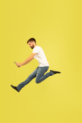 Fototapeta na wymiar Full length portrait of happy jumping man isolated on yellow background. Caucasian male model in casual clothes. Freedom of choices, inspiration, human emotions concept. Takes video for vlog or