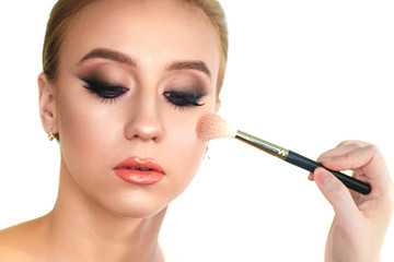 Makeup artist applies blush and powder on the face of the client woman with a brush