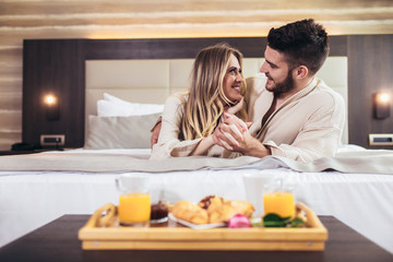 Obraz na płótnie Canvas Young happy couple having breakfast in luxury hotel room.