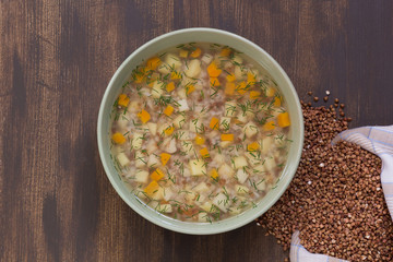 Top view of buckwheat soup in green bowl on brown background