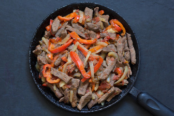 Top view of cooked liver with vegetables on frying pan on black background
