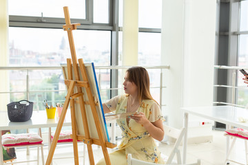 Art class, drawing and creativity concept - Female student sitting in front of easel with palette and paintbrush