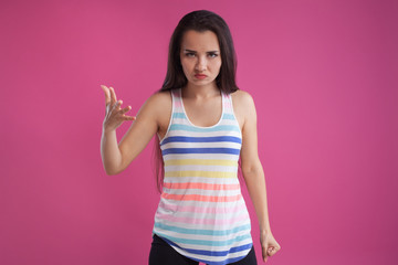 Obraz na płótnie Canvas Brunette woman with long hair, dressed in colorful striped shirt, posing against pink studio background. Sincere emotions. Close-up.