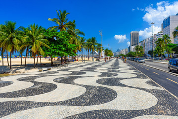 View of Copacabana beach with palms and mosaic of sidewalk in Rio de Janeiro, Brazil. Copacabana beach is the most famous beach in Rio de Janeiro. Sunny cityscape of Rio de Janeiro