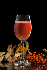 Rowan juice in a glass on a black background with a bunch of mountain ash stands on a mirror surface
