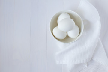 White eggs in a plate on a towel stand on a white wooden table with place for text