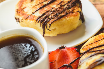 Pancakes with strawberries chocolate and coffee on a wooden table