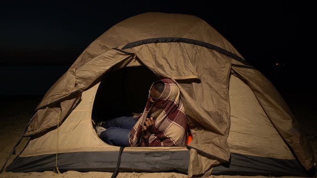 Homeless afro-american man warming up with plaid in tent, loan debtor lost house