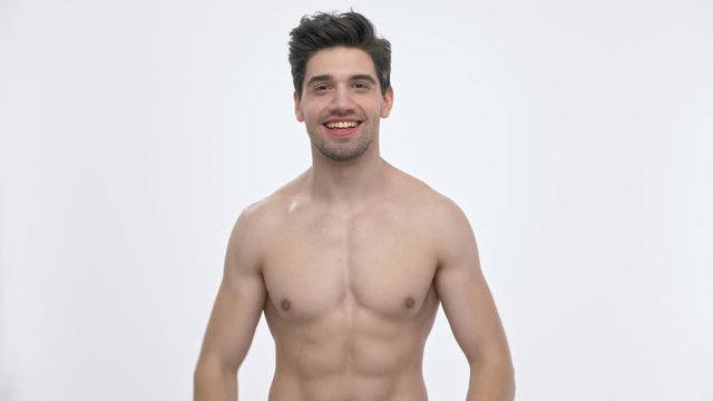 Happy young brunette man with naked torso screaming and making winner gesture with hands while looking at the camera over white background isolated