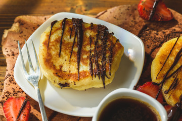 Pancakes with strawberries chocolate and coffee on a wooden table