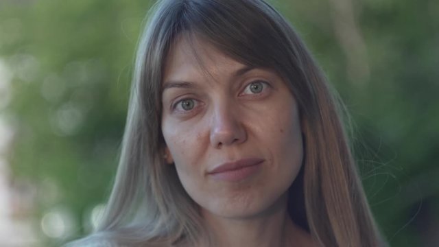 girl without makeup looks at the camera on a background of green foliage. natural female beauty
