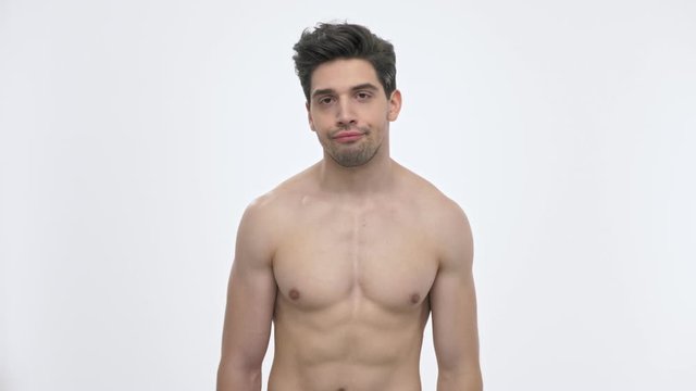 Exhausted young brunette man with naked torso feeling tired and wiping sweat from forehead while looking at the camera over white background isolated