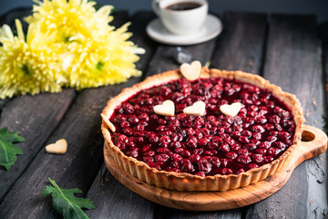 cherry tart with heart shaped decor, on a dark wooden backdrop, golden daisy and cup of coffee on background