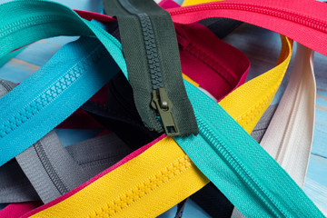 Pack lot of colorful plastic and metal zippers stripes with sliders pattern for handmade sewing tailoring on the blue painted wooden background close up selective focus © vitalis83