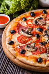 Pizza with tomato, olives, champignons, ham and cheese on round wooden plate