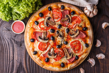 Pizza with tomato, olives, champignons, ham and cheese on round wooden plate
