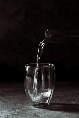 Water poured from the bottle into a glass cup on a black background