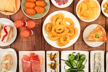 Spanish tapas, an overhead photo of a variety of snacks. Gazpacho, squid rings, tortilla, jamon, cheese etc, shot from the top on a dark rustic wooden background