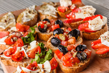 Assorted bruschetta with tomato, olives, camembert, blue cheese, lettuce, pear, honey on wooden board