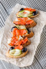 Bruschetta with smoked salmon, fresh cucumber, black olives and camembert on crumpled baking paper