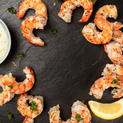 Cooked shrimps with a Caesar sauce and lemon, shot from above on a black background, forming a...