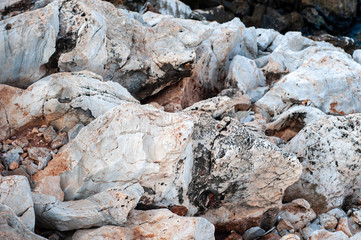 Raw stone on the coast of the Aegean. Texture of weathered, cracked stone. Gray with orange and black veins.