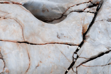 Raw stone on the coast of the Aegean. Texture of weathered, cracked stone. Gray with orange and black veins.