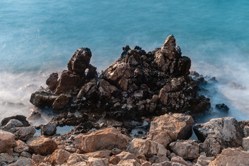 Fototapeta na wymiar Sharp stones and rocks in the turquoise, blue sea. Beautiful seascape. Aegean coast in Turkey at sunrise. Bodrum.