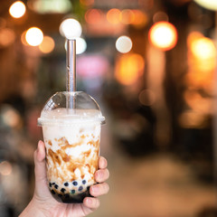 Young girl is holding and showing a cup of brown sugar flavored tapioca pearl bubble milk tea in...