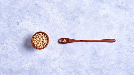 pine nut in a wooden bowl whith wooden spoon on a blue and white background top view