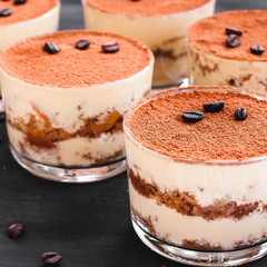 gourmet tiramisu dessert in a glass sprinkled with cocoa and decorated with coffee beans on a dark background, luxury dessert
