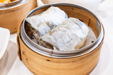 Delicious Lo Mai Gai dim sum, fresh steamed glutinous rice with chicken roll wrapped by lotus leaf in bamboo steamer in hong kong yumcha restaurant.