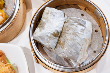 Delicious Lo Mai Gai dim sum, fresh steamed glutinous rice with chicken roll wrapped by lotus leaf in bamboo steamer in hong kong yumcha restaurant.